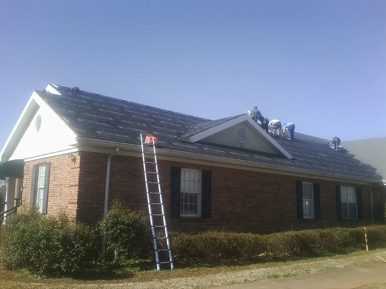 Crew tearing shingles off a brick ranch roof with a ladder set — Emergency Roof Repair work by our crew in Marblehead