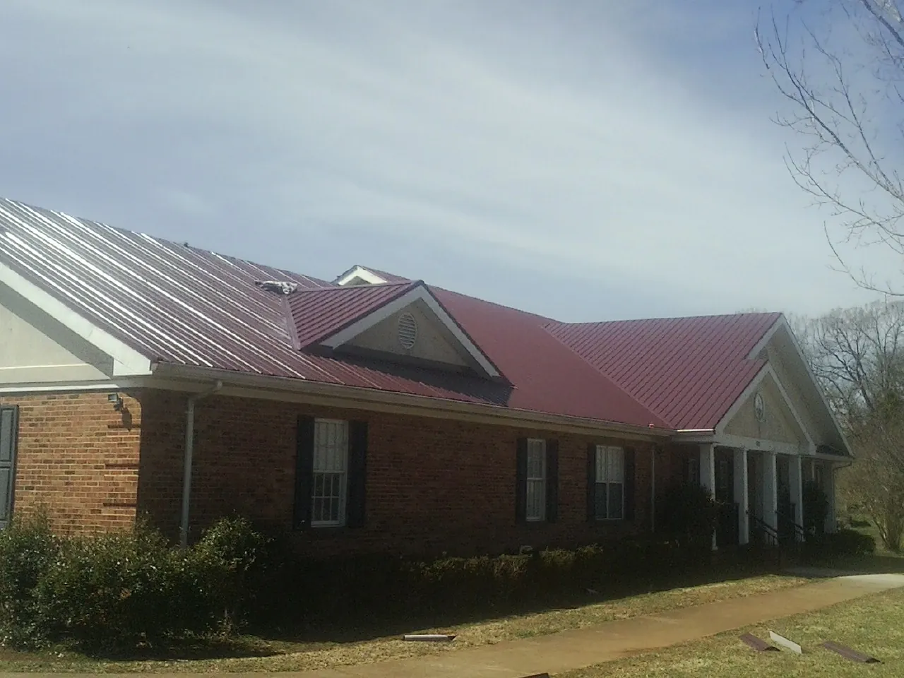 Red metal roof with gabled entries on a long brick building, from a Hail Damage Roof Repair job in Marblehead