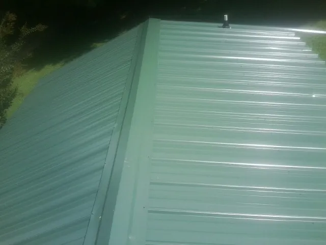 New green metal panels meeting at the ridge of a roof — Flat Roof Repair work by our crew in Marblehead