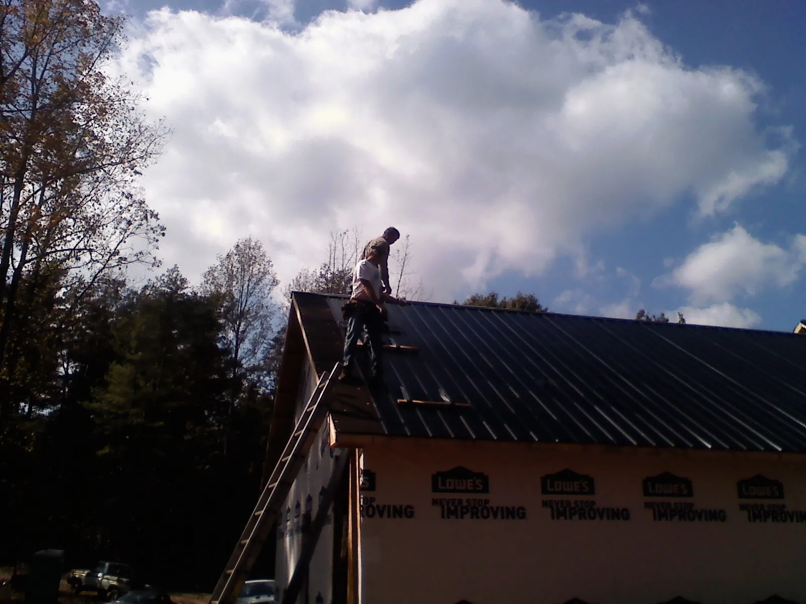 Roofer fastening dark metal panels high against a cloudy sky, from a Roof Inspection job in Marblehead