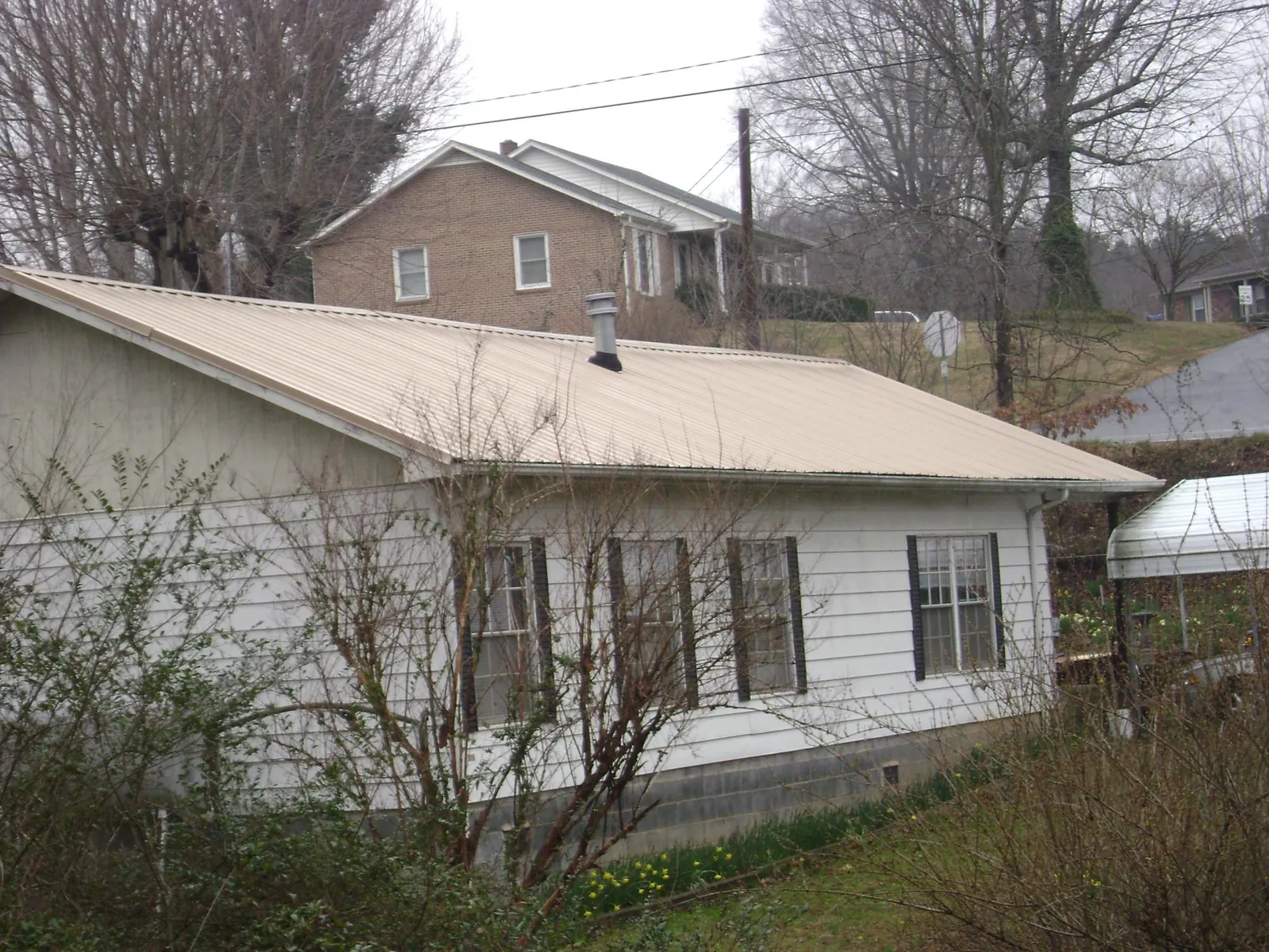 Tan metal roof on a white sided house set into a hillside — Commercial Roofing by Roofing Brothers in Marblehead